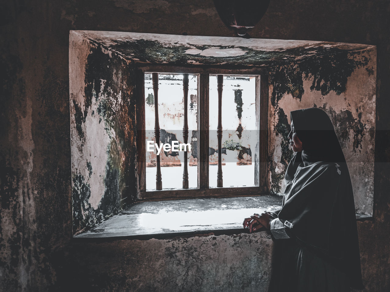 Rear view of girl standing against window in abandoned building