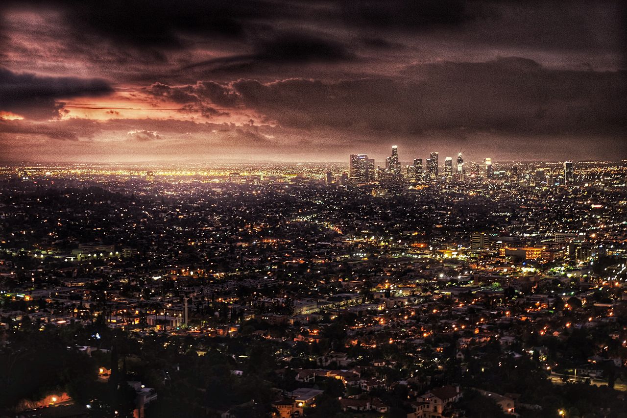 Scenic view of illuminated cityscape against cloudy sky