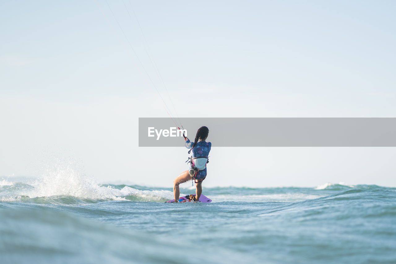 Back view of fit female kite surfer in swimsuit ridding waves in sea on sunny day in summer