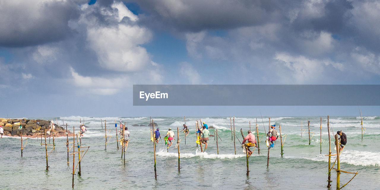 Men fishing in sea against cloudy sky