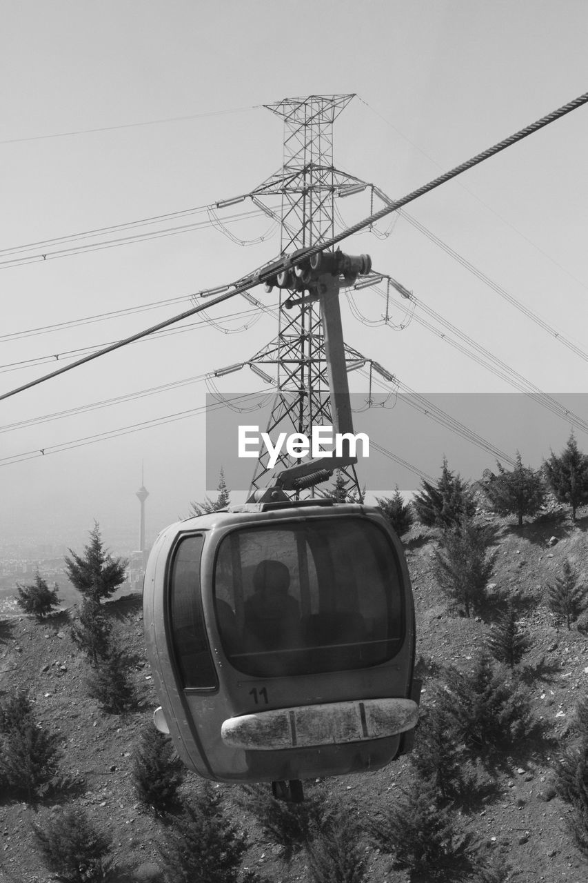 Low angle view of overhead cable car and electricity pylon against sky