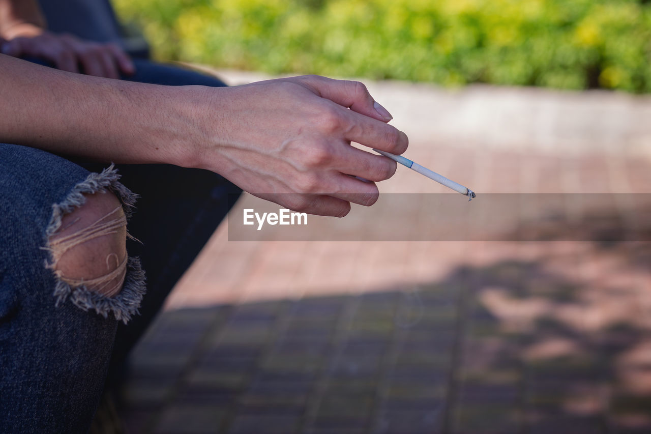 Cropped image of man smoking cigarette while sitting outdoors