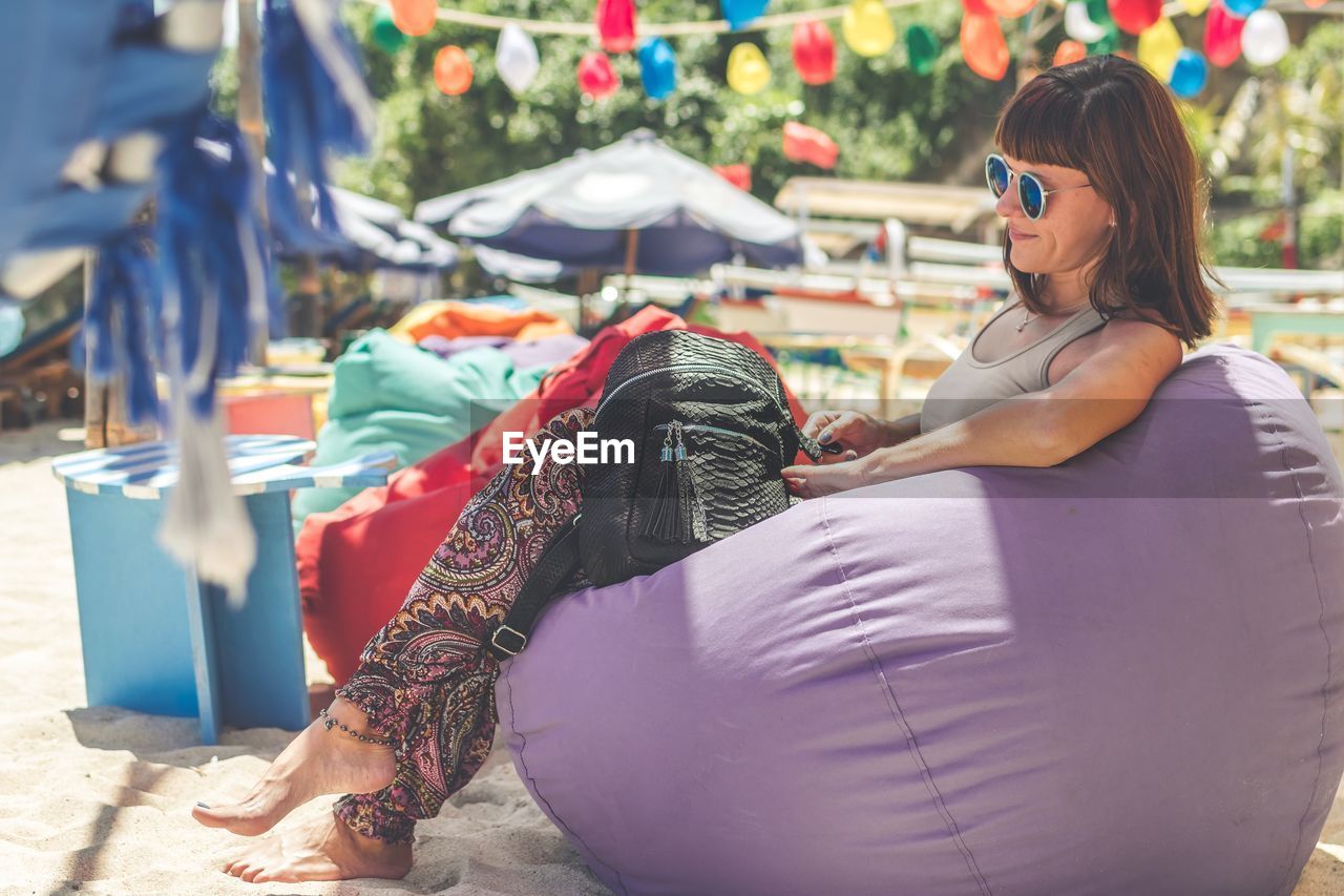 Smiling young woman wearing sunglasses while sitting on bean bag at beach