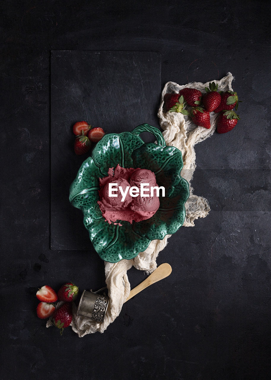 Top view of scoops of tasty ice cream in plate placed on table with fresh strawberries and napkin