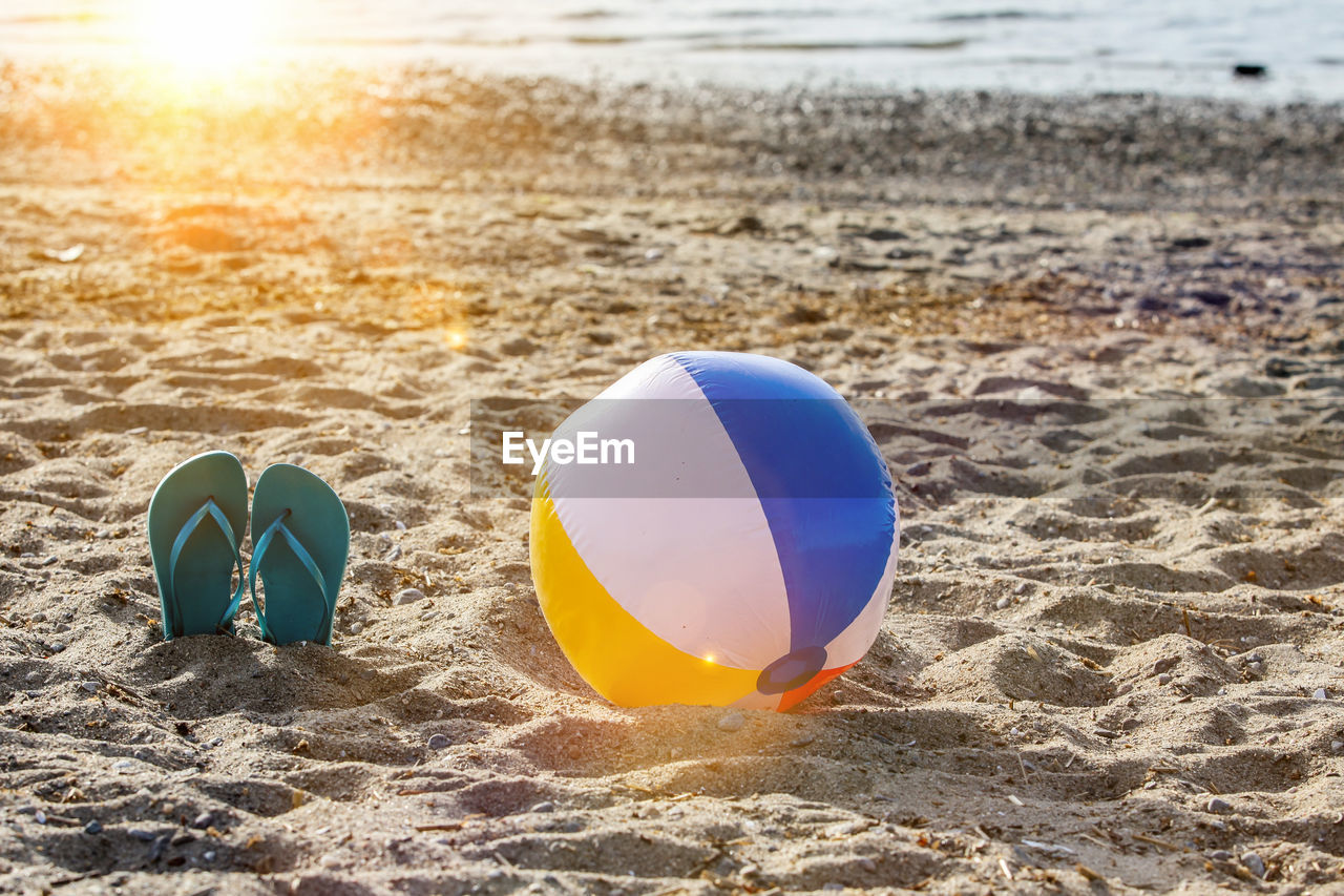 Flip flops on beach sand with beach ball and sun