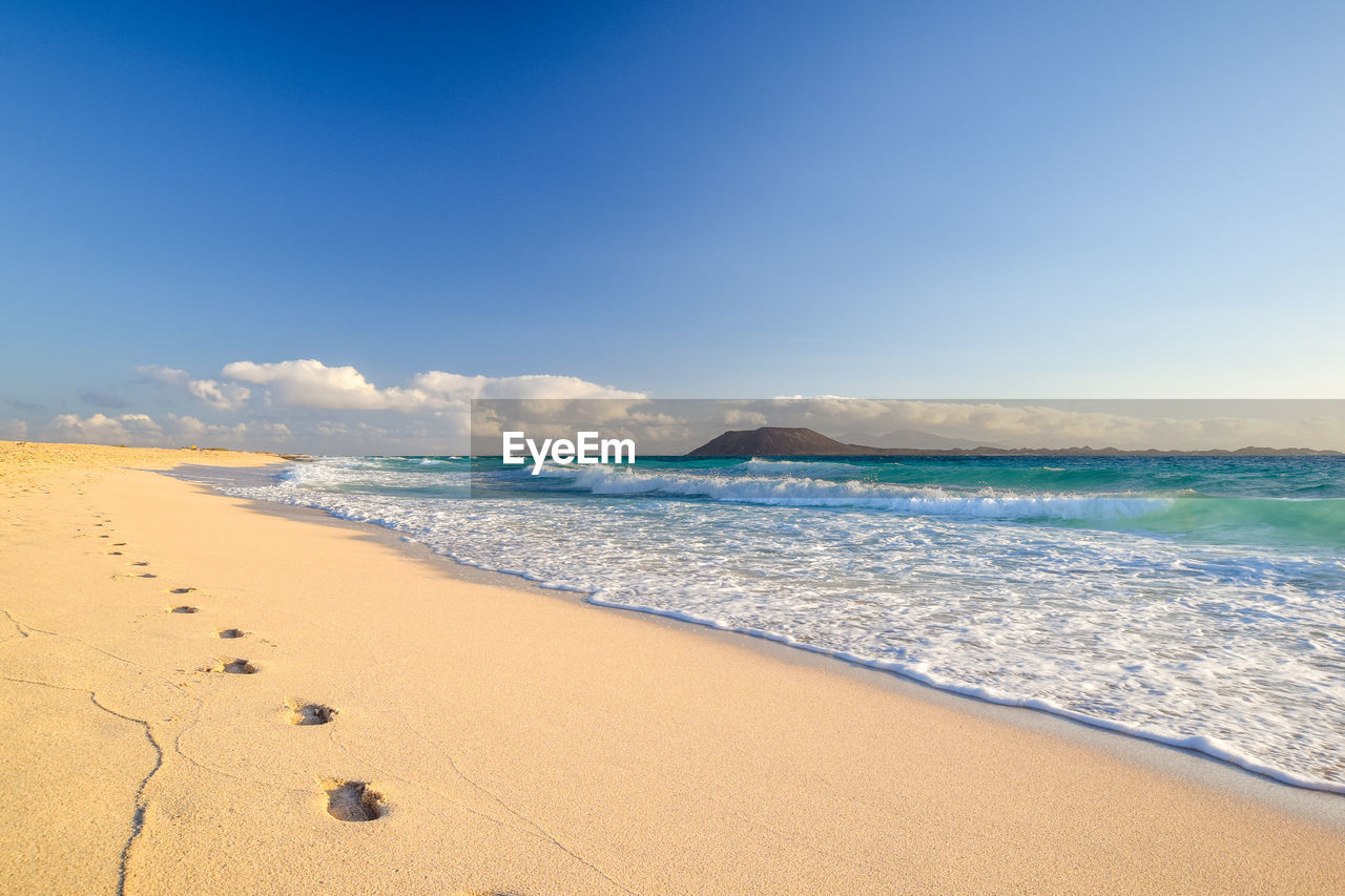 Lobos and lanzarote seen from corralejo beach, fuerteventura, canary islands. footprints in sand.	