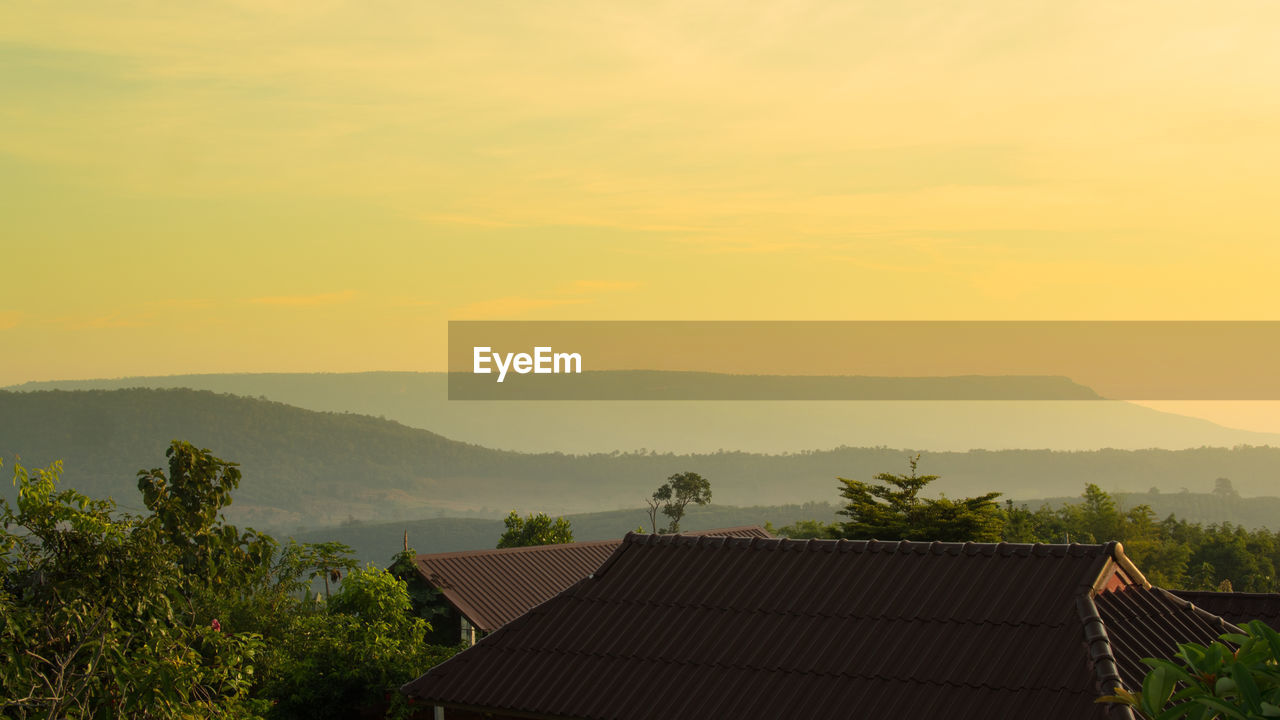 High section of houses amidst trees against sky during sunset