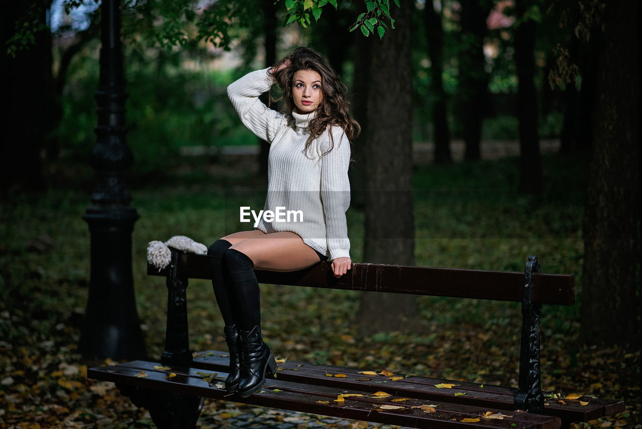 Woman looking away while sitting on bench in park