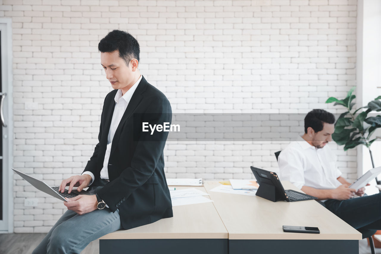 YOUNG MAN USING PHONE WHILE SITTING IN OFFICE
