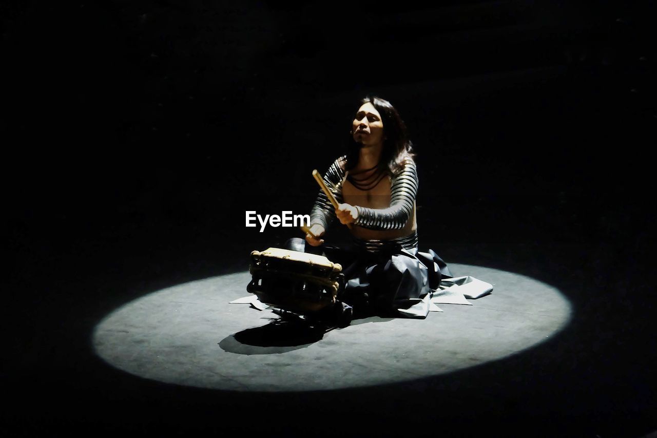 YOUNG WOMAN SITTING AGAINST BLACK BACKGROUND AT NIGHT