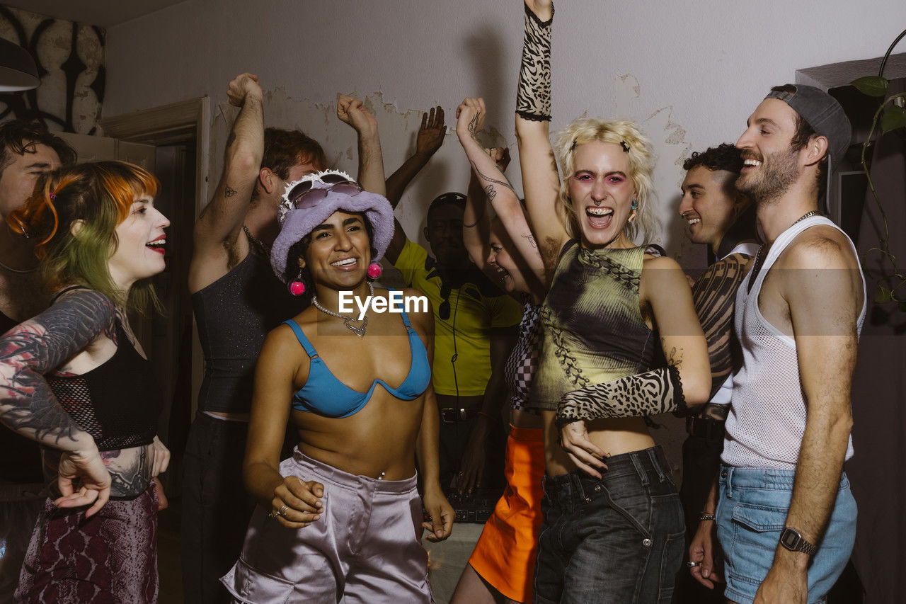 Carefree group of non-binary friends dancing at party in apartment