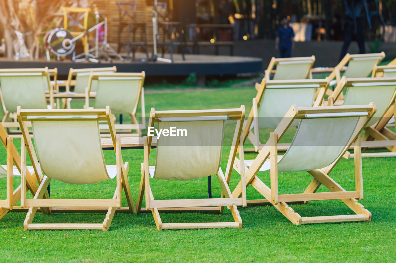 Many white deck chairs with tables for dinner in lawn is surrounded by shady green grass 