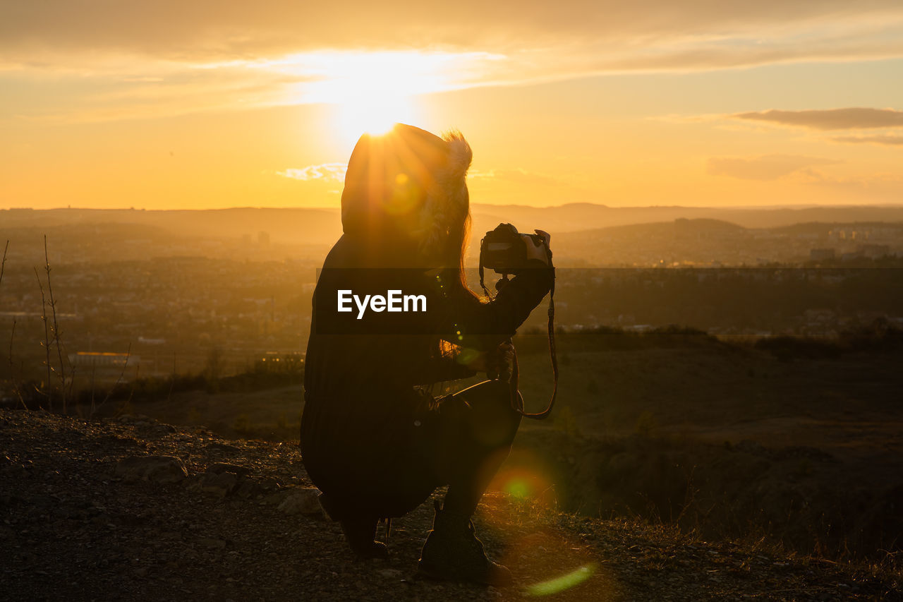 Silhouette woman photographing against sky during sunset