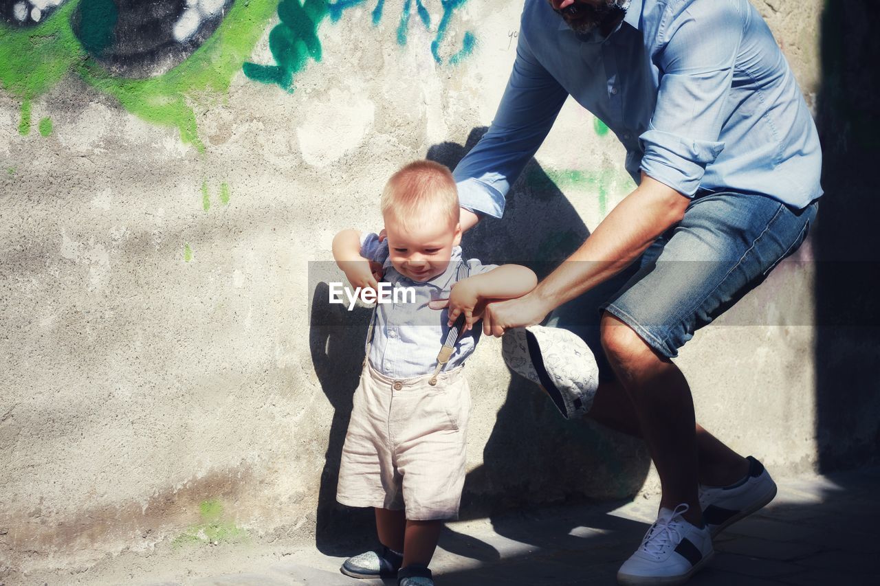 Midsection of father holding sin by wall outdoors