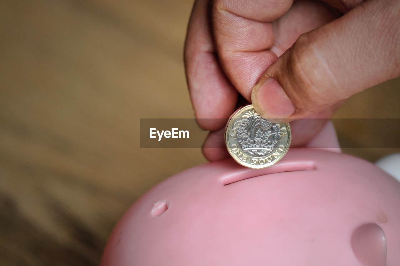 Close-up of hand holding coin over piggy bank