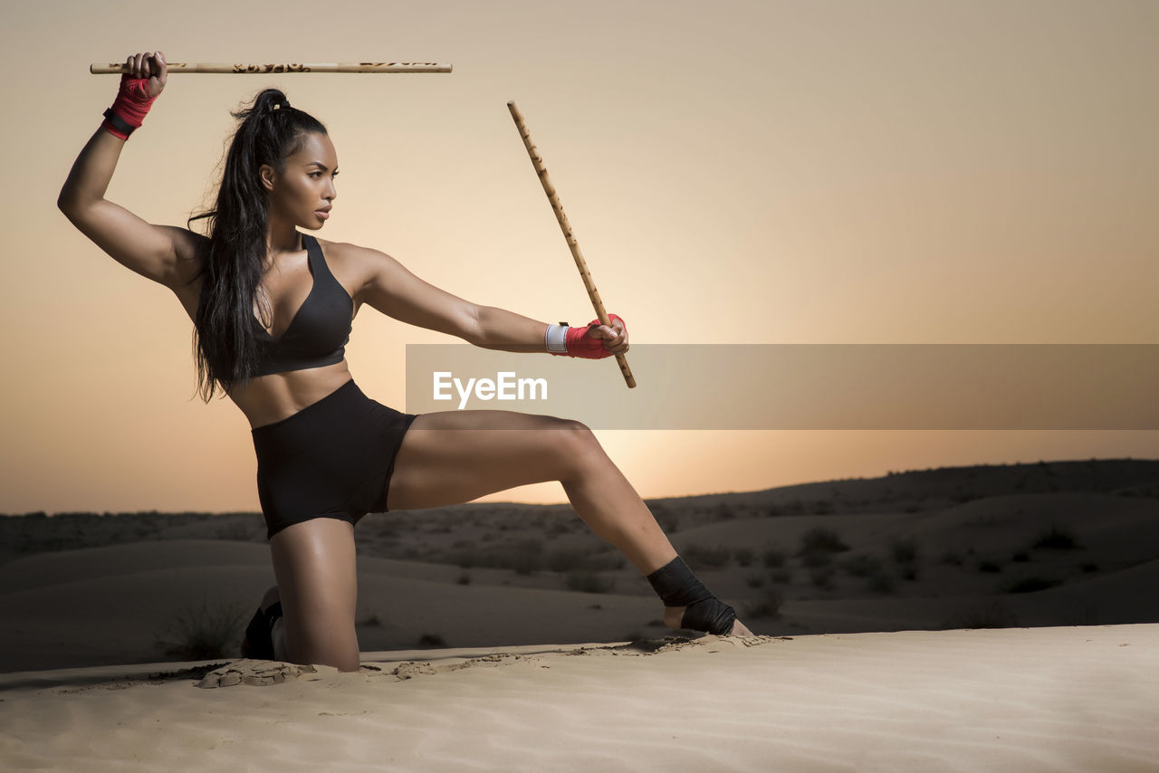 Young woman exercising on sand against sky