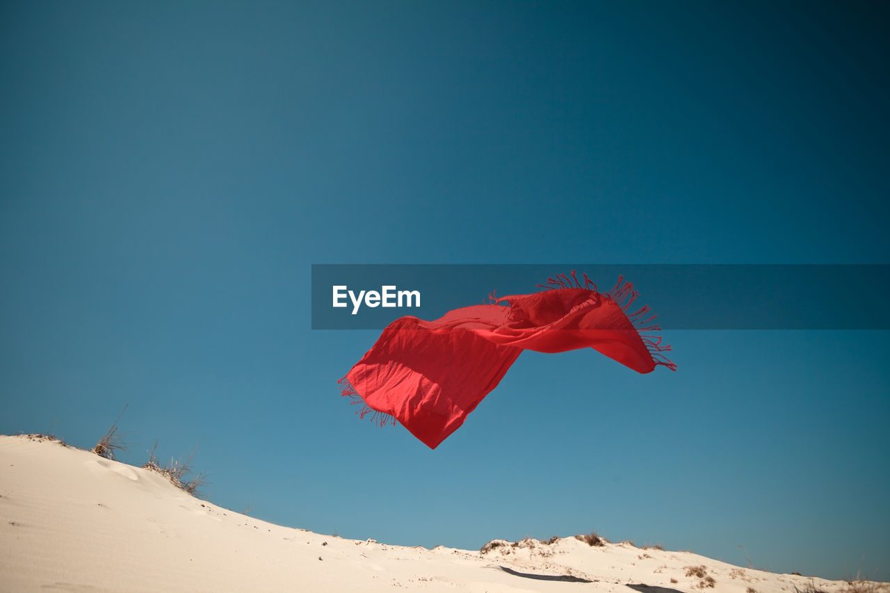 Low angle view of red scarf flying over sand against clear blue sky