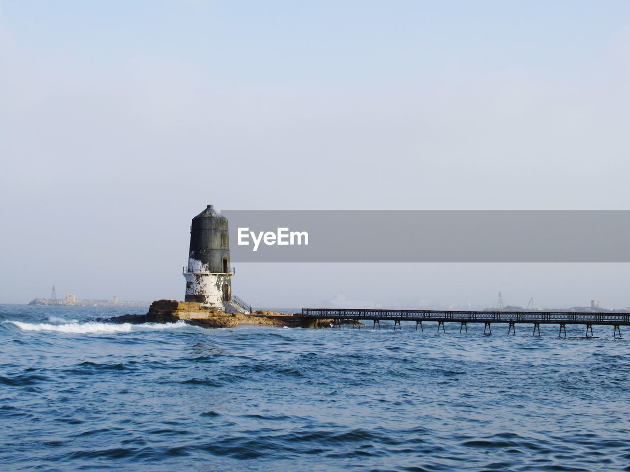 Lighthouse by sea against clear sky