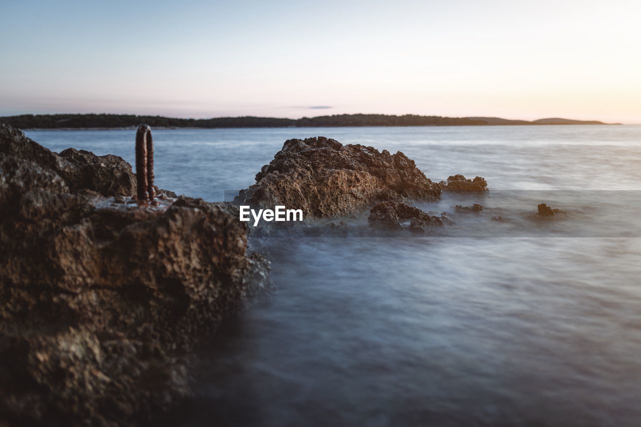 Rocks on beach against sky during sunset