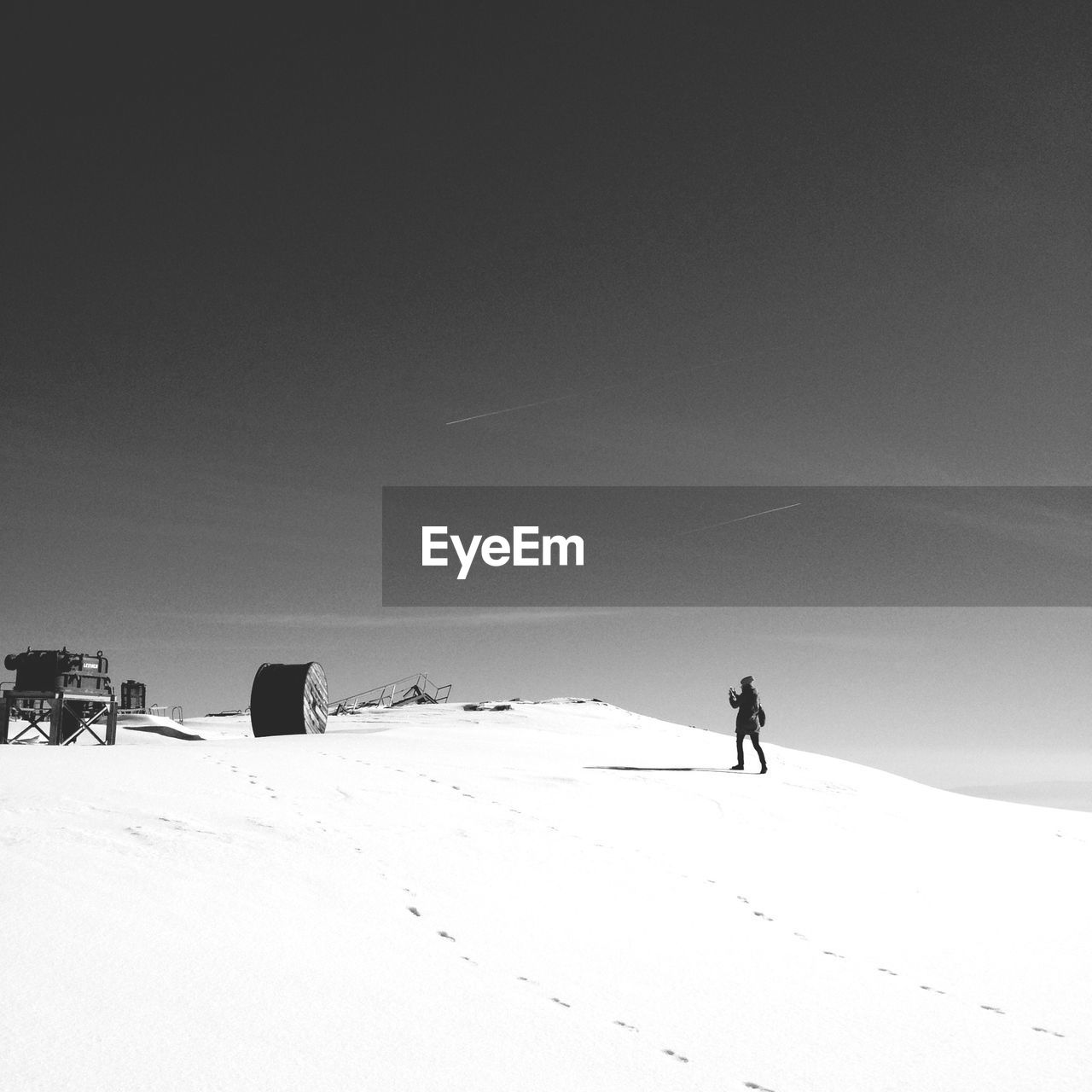 Woman photographing obsolete factory on snowy landscape against sky