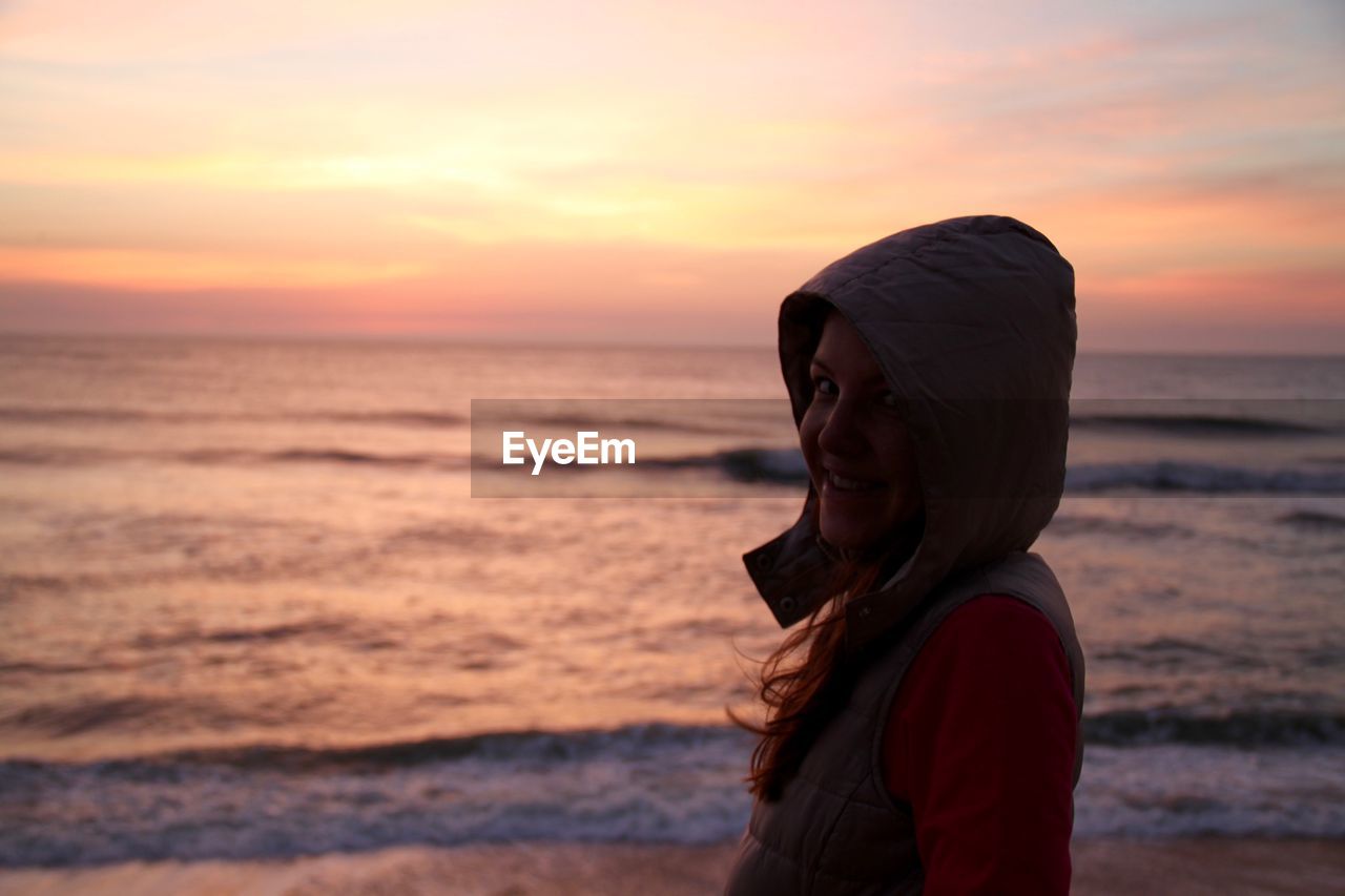 Portrait of smiling woman standing on shore at beach during sunset