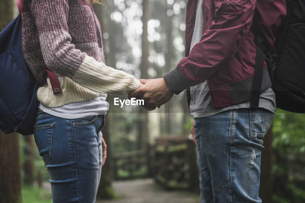 Midsection of couple holding hands in forest