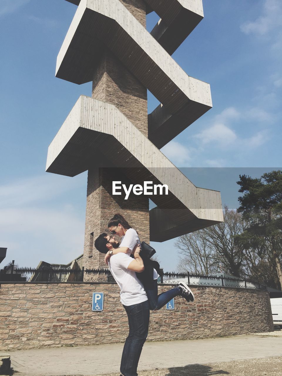 Man carrying woman standing against built structure in city