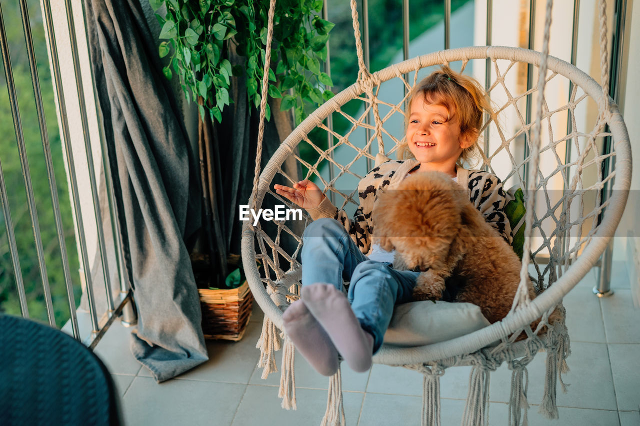 Happy little girl, child hugging with a smile her pet, poodle dog at home on balcony spring, summer