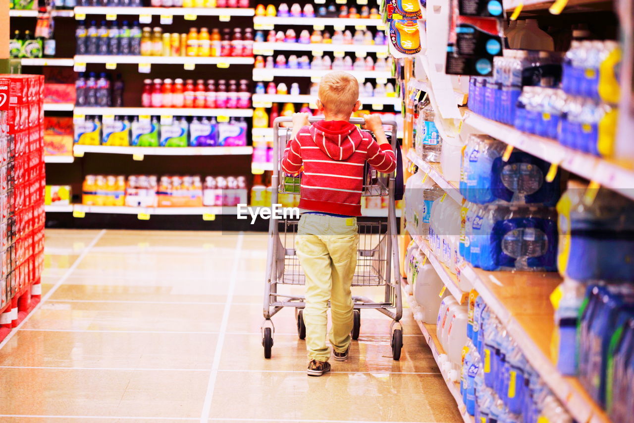 Rear view of boy with shopping cart walking in supermarket