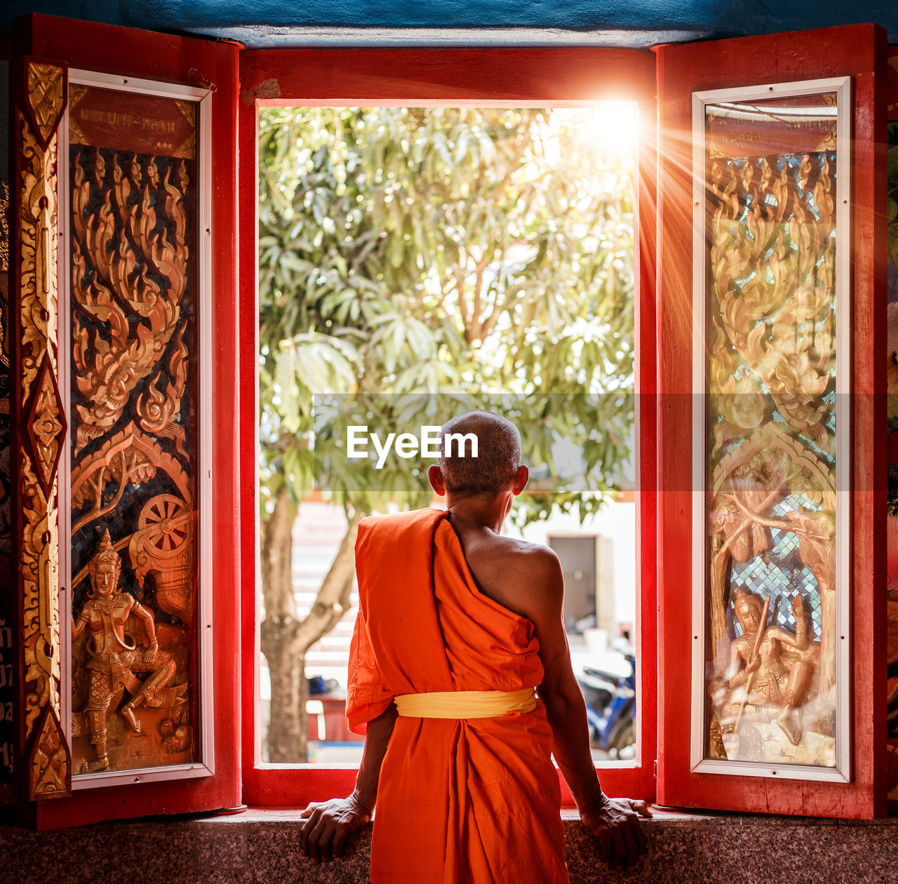 Rear view of monk looking through window at temple