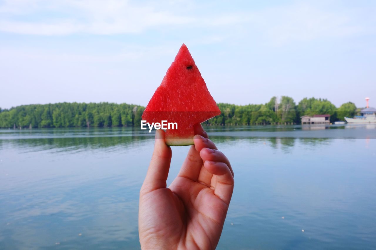 Close-up of hand holding watermelon against lake