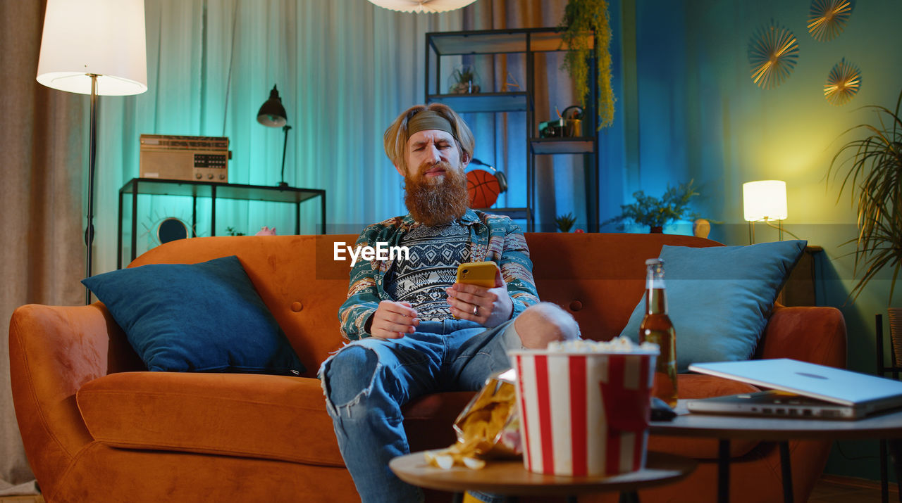 young woman using phone while sitting on sofa at home