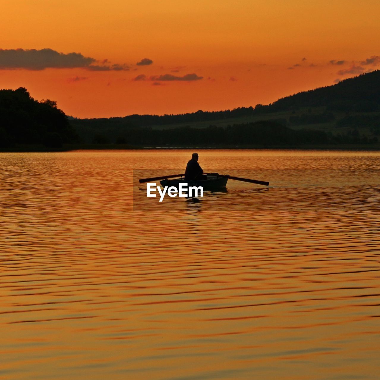 Silhouette man on boat at lake against sky during sunset