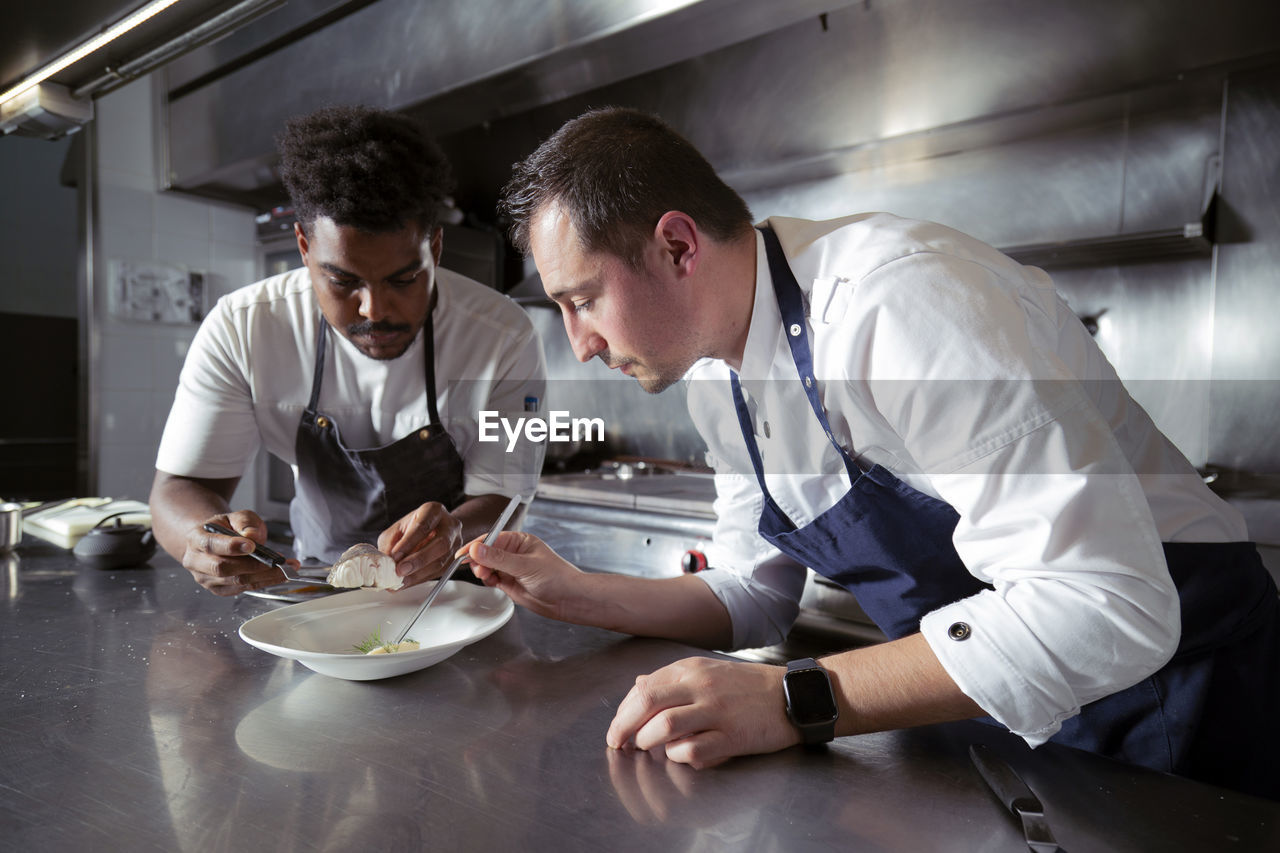 Concentrated multiethnic professional cooks preparing meal with slice of fish on ceramic plate in restaurant while working together