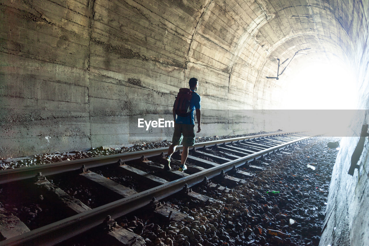 REAR VIEW OF A MAN WALKING ON RAILROAD TRACK