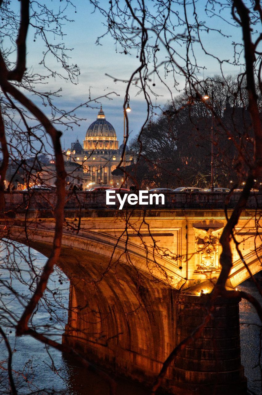 Bare trees, buildings and a bridge against sky during sunset