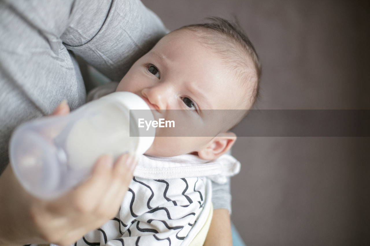 Midsection of mother feeding milk to baby boy with bottle at home