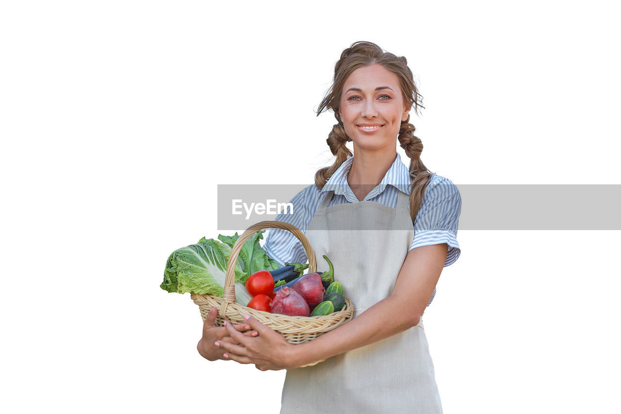 PORTRAIT OF SMILING YOUNG WOMAN STANDING AGAINST WHITE BACKGROUND