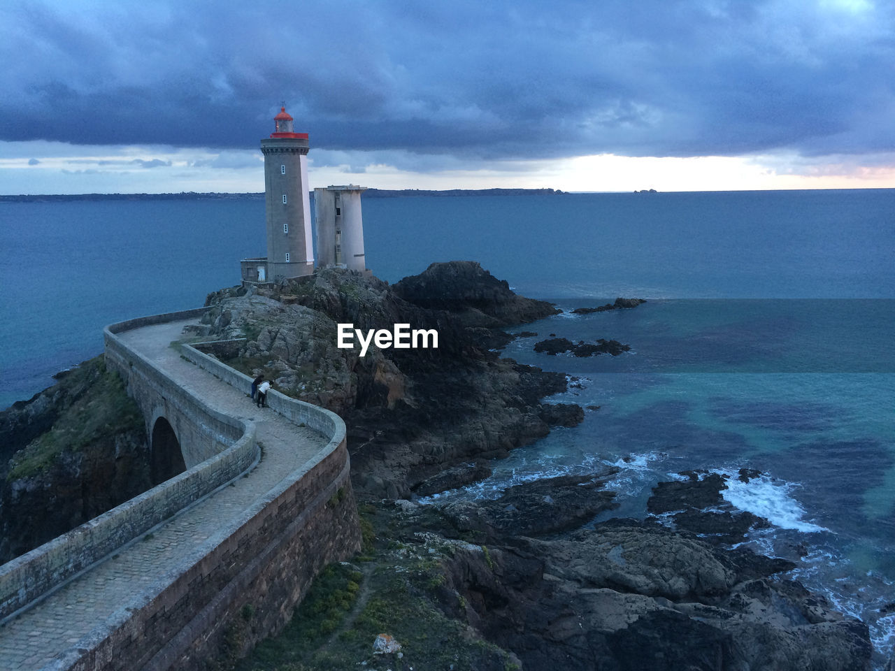 Lighthouse by calm blue sea against sky