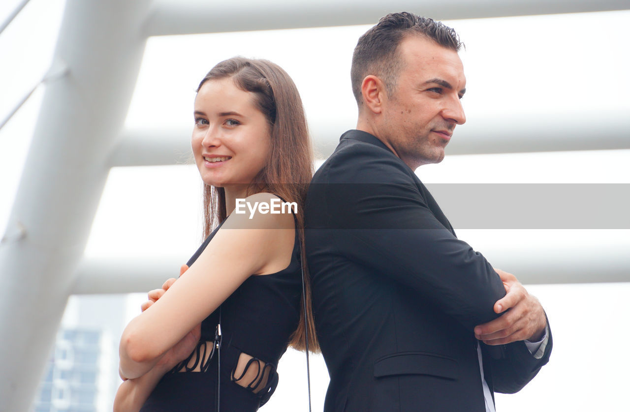 Side view of business couple standing back to back in city