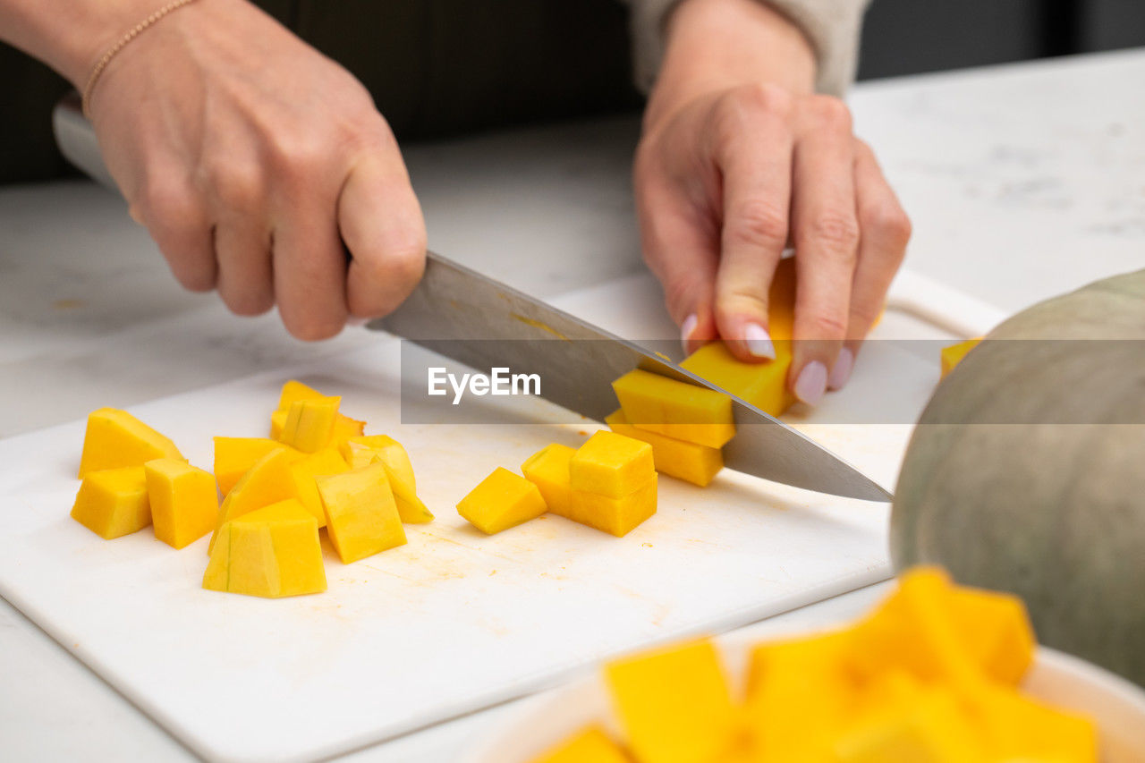 hand, food, food and drink, indoors, adult, cutting, kitchen, occupation, chopping, freshness, men, one person, kitchen knife, cutting board, healthy eating, produce, business, domestic room, preparing food, close-up, home, yellow, selective focus, working, domestic kitchen, holding, baked, wellbeing