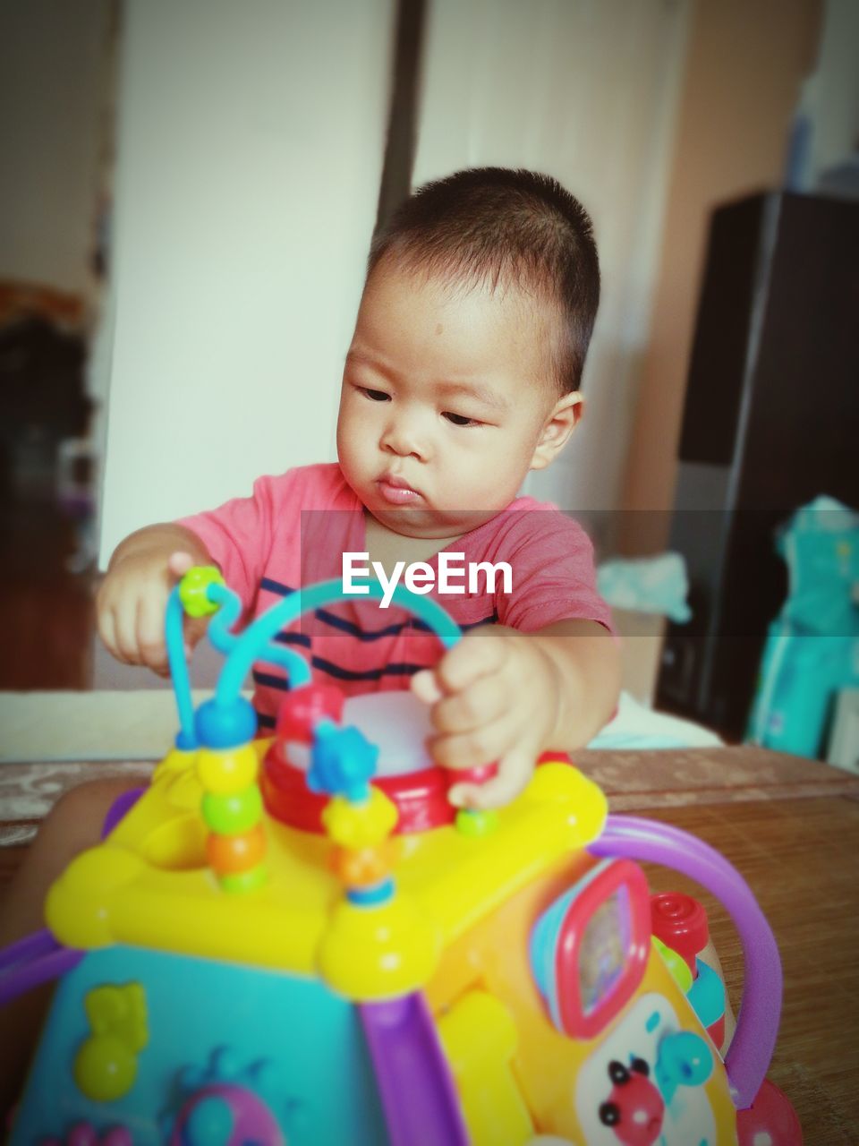 Cute baby boy playing with toys while sitting on table at home