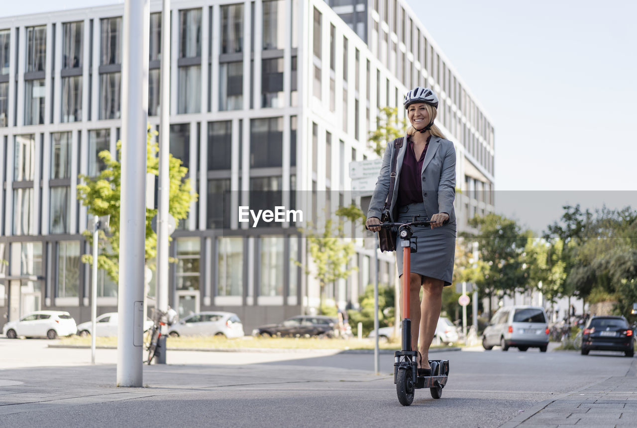 Happy businesswoman riding electric scooter on the street