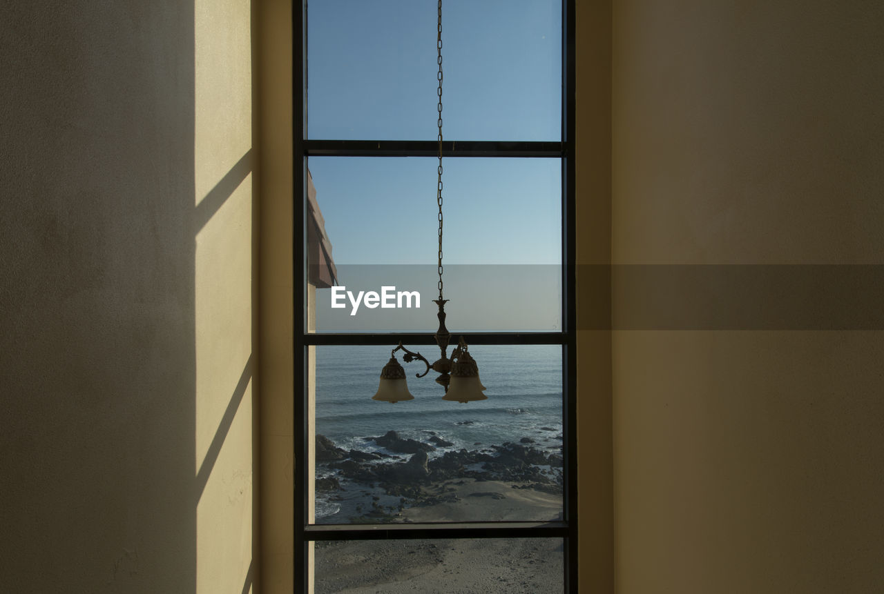 Pendant light hanging by glass window at home with sea in background