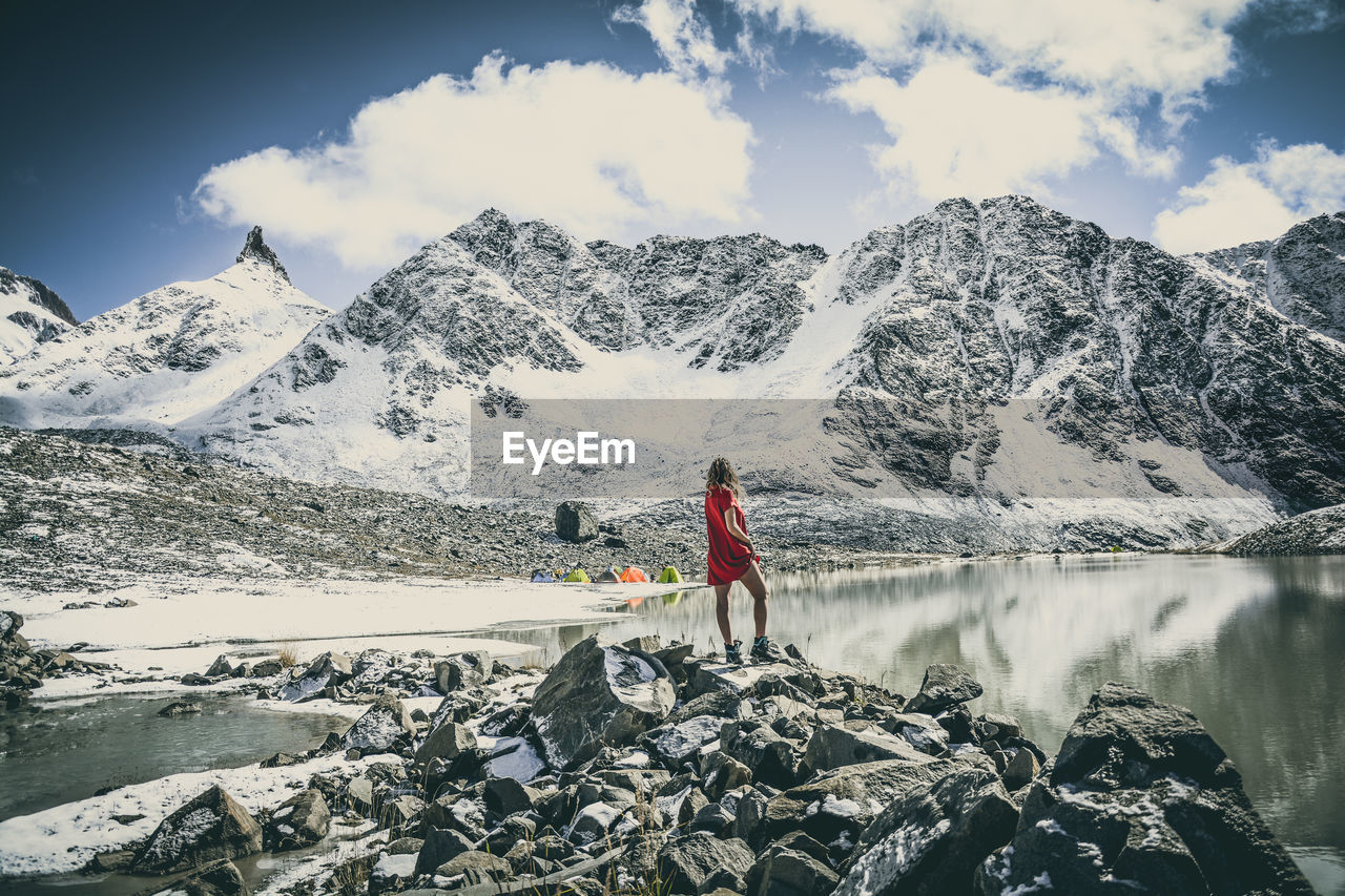 Rear view of woman standing against snowcapped mountains on rock