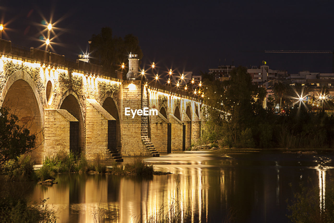 ILLUMINATED BRIDGE OVER RIVER AGAINST SKY