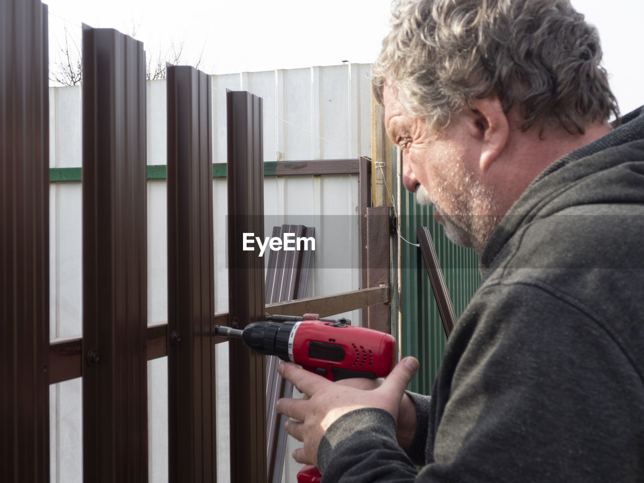 Side view of senior man drilling metallic fence