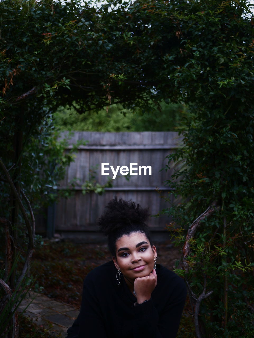 Portrait of smiling young woman sitting against trees in backyard