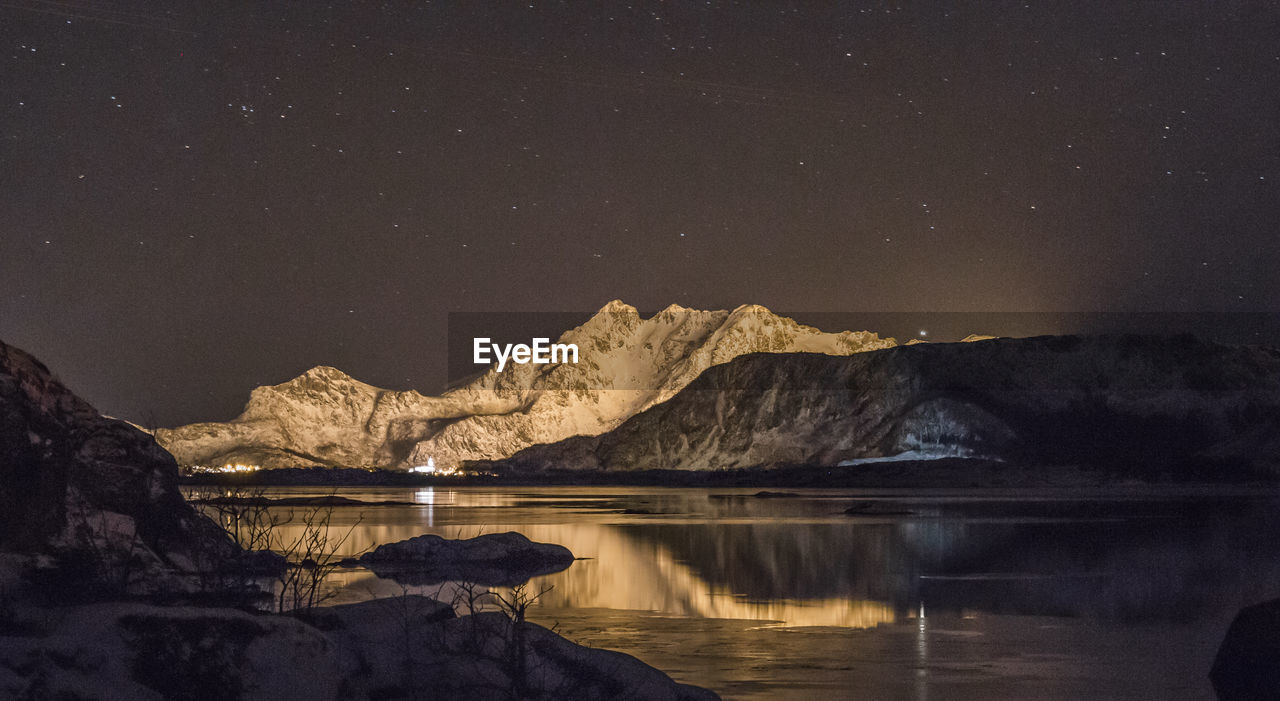 SCENIC VIEW OF LAKE BY MOUNTAINS AGAINST SKY AT NIGHT