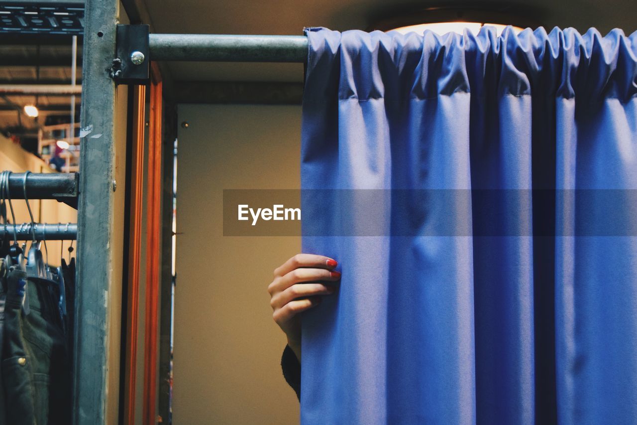 Cropped hand of woman closing blue curtain of changing room